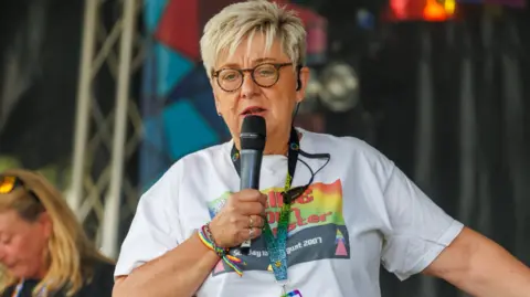 Doncaster Pride/Wayne Sables Woman with short blonde hair and glasses on stage with a microphone