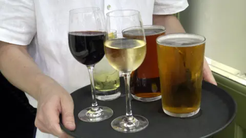 A person in a white shirt carrying a black tray of drinks with five glasses.