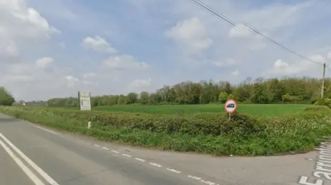 General view of junction with green bushes running along and blue sky.