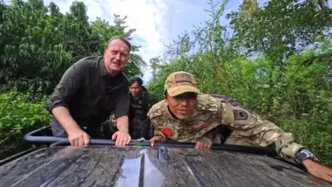 Sommerville and the young rebels on an open top vehicle driving through jungle