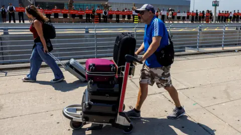Male Grepers in a blue-birke--birke-up shirt with a trolley point stacked by the baggage next to the women with a long feather, jeans hill and back