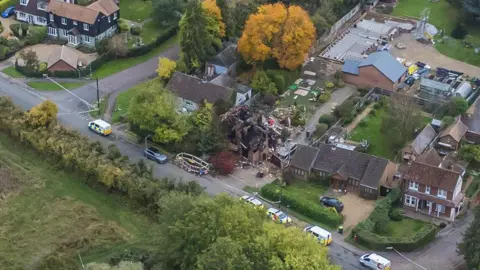 Ant Saddington/BBC A drone shot of a destroyed detached house close to other large houses that are untouched. Police tape and emergency vehicles fill the road outside.