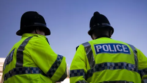Getty Images Two police officers in high-vis jackets stand side by side but facing away from the camera. They are both wearing helmets.