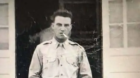 Catharine Mosbarger A sepia toned picture of a young man wearing a military uniform. He is smoking a cigarette which he is holding in his mouth. The man has curly dark hair and appears to be squinting at the camera.