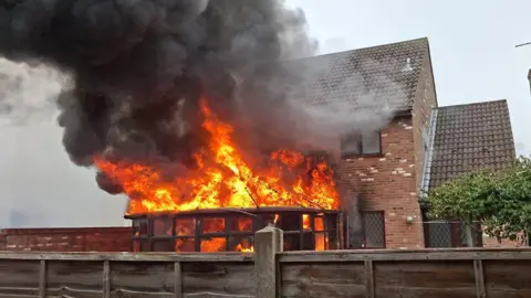 Emma Parker A large fire with black smoke billowing above it. The fire has filled the conservatory and appears to have spread to the house. 