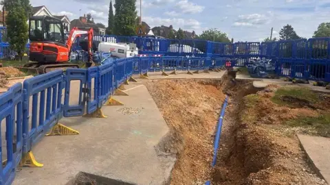Photo of the ground, blocked off by blue fencing where a sinkhole is.