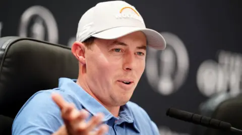 PA A man with a blue polo top and beige cap on sat in front of a microphone.