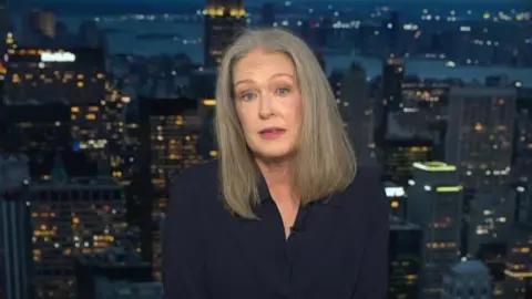 Author Amy Wallace sitting in front of a set showing a city skyline