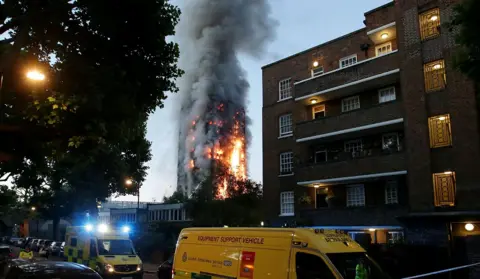 AFP Emergency vehicles are seen responding on a dark street as fire and smoke engulf the Grenfell tower in the background, in London on 14 June