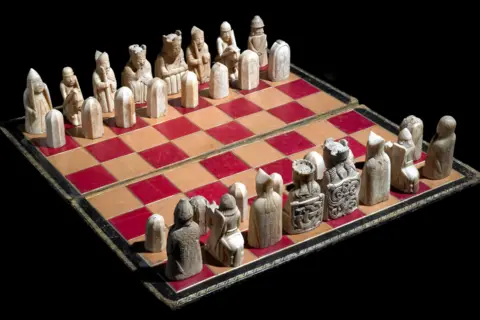 The Trustees of the British Museum Images shows Lewis chess pieces, made of ivory from the 12th Century - on red & beige board