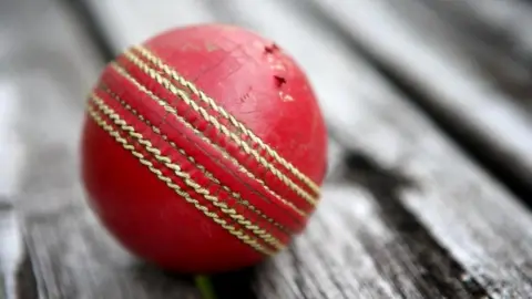 PA Media Close-up image of a traditional red cricket ball on a black-and-white background