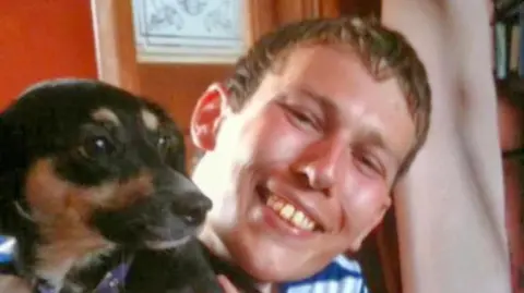Bedfordshire Police Dean Fountaine: a man with short brown hair wearing a blue and white-stripped top. He is smiling. The head of a black and brown dog is to his left.