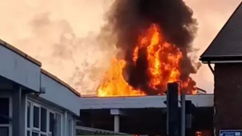 Fire at Paignton station. Red flames and billowing black smoke can be seen over a flat roof.