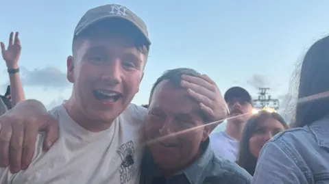 Leah Bonner Paul wearing a cap is seen with his arm around his dad who looks emotional.
