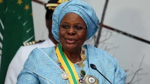 Namibian president Netumbo Nandi-Ndaitwah is seen wearing a light blue dress and matching head wrap while speaking at an event