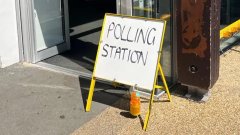 A handwritten polling station sign stood outside an open set of automatic doors.