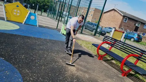 IRC Romeo Mustata with a broom, sweep the ground inside a children's play area.