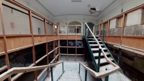 Qays Najm/BBC Part of the inside of County Hall, which is in need of refurbishment. The photo shows a large open stairwell with wooden panels throughout the room that need replacing.
