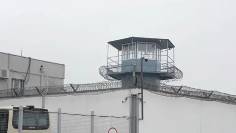 Rayhan Demytrie/BBC Another look at the outside of the prison. The watchtower in the centre with barbed wire topped walls extending on either side.