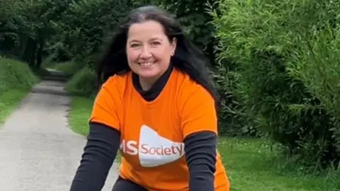 Woman on a bike on the Camel Trail at Wenford Bridge wearing a bright orange multiple sclerosis t-shirt