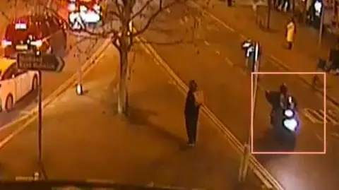 Grainy CCTV image of a road junction in the dark, with a moped and rider circled 