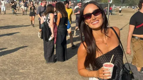 Lauren Macpherson Lauren Macpherson stands on a festival field. People can be seen in crowds behind her. She holds a pink drink in a plastic cup in her left hand and has a black bag on her shoulder. She wears black sunglasses, has brown long hair and smiles at the camera. 