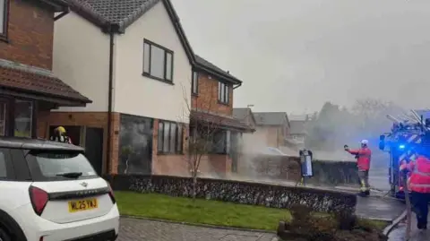 Kaela Rigg The outside of Kaela's house. Smoke is visible as firemen attempt to extinguish the fire.