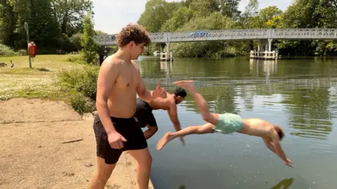 Three young men in swimming shorts dive into the River Thames