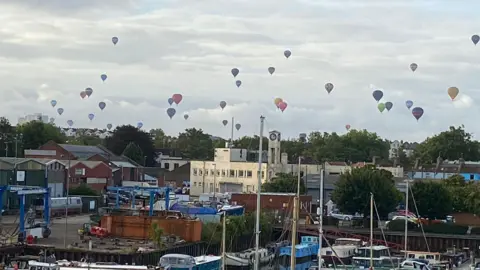 Rachel Harries Balloons flying over a harbour with many boats in the water.