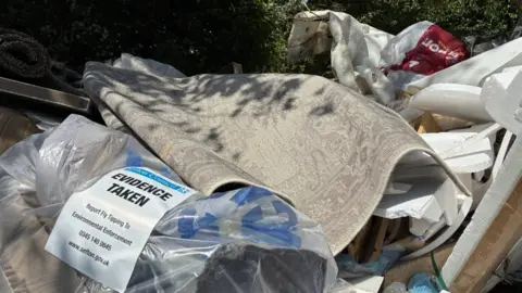 Close up of lots of rubbish with a paper tag stuck to it saying 'Evidence taken'.
