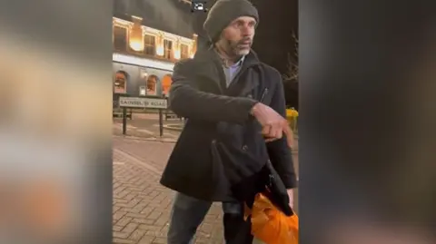 BTP Photo of man in black jacket and grey hat with orange carrier bag