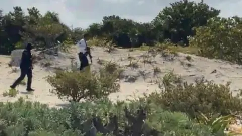 Colin Nulty Armed officers patrol the beach in a search for suspects