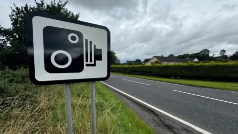 A speed camera sign on the side of a single carriageway road