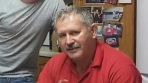 Family photo Mike O'Leary - A man in a red polo shirt with grey hair and a grey moustache