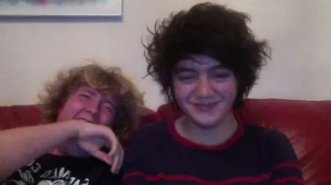 Josh Law/Ben Sadler A graint photo of Josh and Ben as young teens, both with big sweeping hair and fringes. They are on a sofa and Josh is smiling, Ben is leaned back laughing.