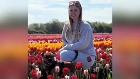 Thames Valley Police/Logan family Jennie Logan with her dog Mouse in a field of ped, while and yellow tulips. She is kneeling on the ground next to Mouse - a Staffordshire bull terrier. Ms Logan is wearing a grey tracksuit.