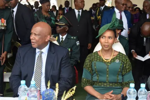Lesotho's King Letsie III, wearing a navy blue suit with a striped tie, next to Queen Masenate Bereng Seeiso, clad in a green dress, at an event