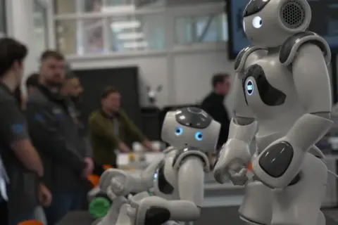 Two small futuristic robots with cute faces in the university lab.