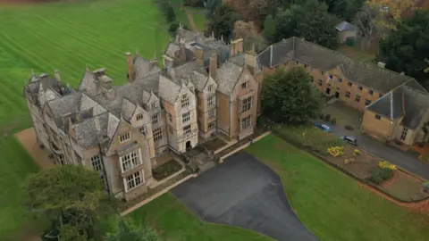 An aerial view of a large historic house surrounded by lawns and trees