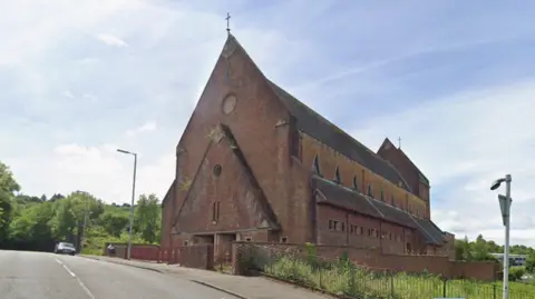 A tall red brick church building on a grassy hill