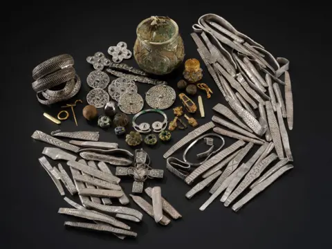 NMS An array of items discovered in a Viking-age hoard in Galloway is spread out on a dark background including an urn, arm rings, bracelets, brooches and other items