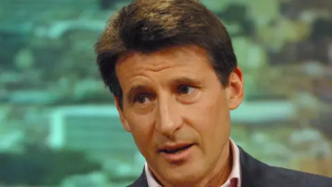 Lord Sebastian Coe, who is wearing a pink shirt and blue blazer, and has short dark hair