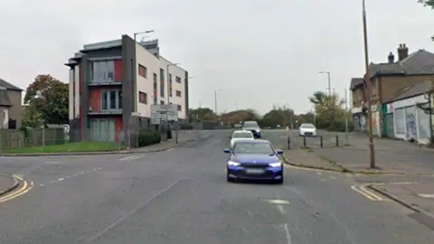 Road with cars on it and flats, houses and shops on either side