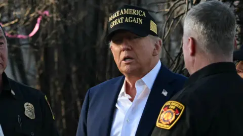 Donald Trump stands in front of fire damage with two members of the fire department