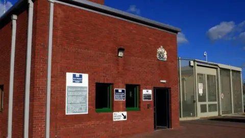 Entrance of HMP Ranby, showing a brick reception building next to a metal mesh gate