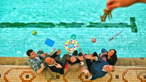 Bramley Baths A group of people sit on the side of a swimming pool and look up towards hanging keys