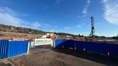 Qays Najm/BBC A construction site with a piling machine behind a fence with "Capital Sky Ltd" on a sign on the gate.