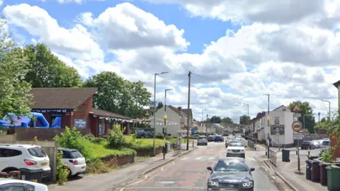 Google Cars drive up and down part of Gorsebrook Road. There is a pub on one side of the road  with bunting up outside.