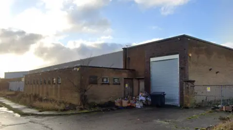 A screengrab of a large brick building with grey shutters.