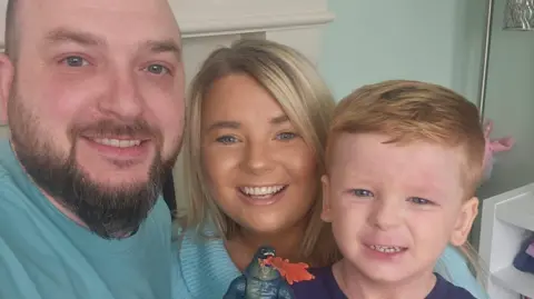 Family Handout A man with a bald head and a beard wearing a green tee shirt smiles at the camera (left)
(Middle) A woman with blonde hair, wearing a green sweatshirt smiles at the camera
(Left) A boy with red hair smiles at the camera, he is wearing a blue top and is holding an action figure up to the camera. 